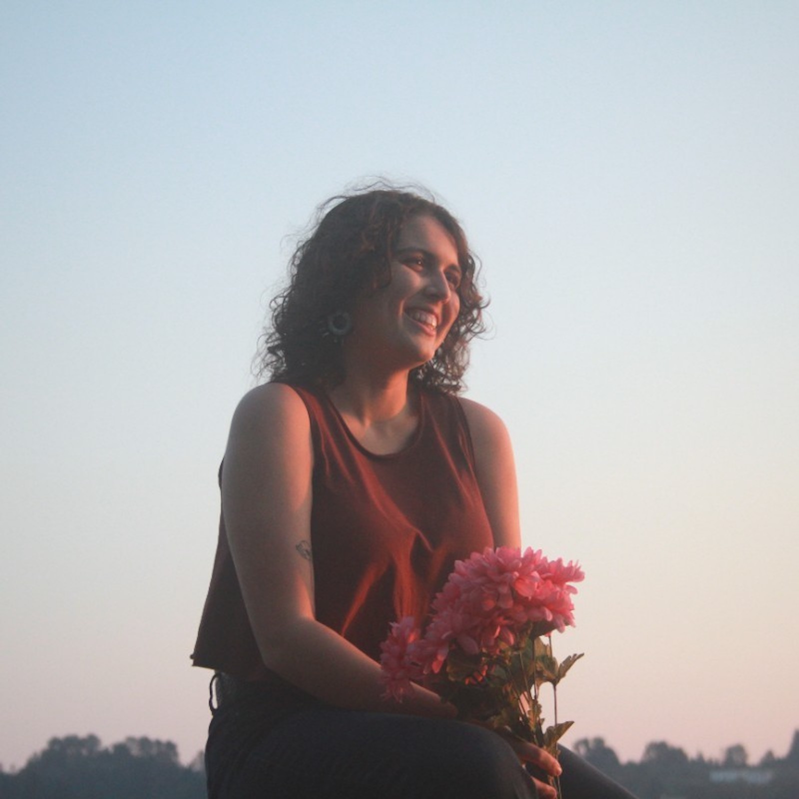 Aysha Dulong, smiling in front of the sunset, holding pink flowers