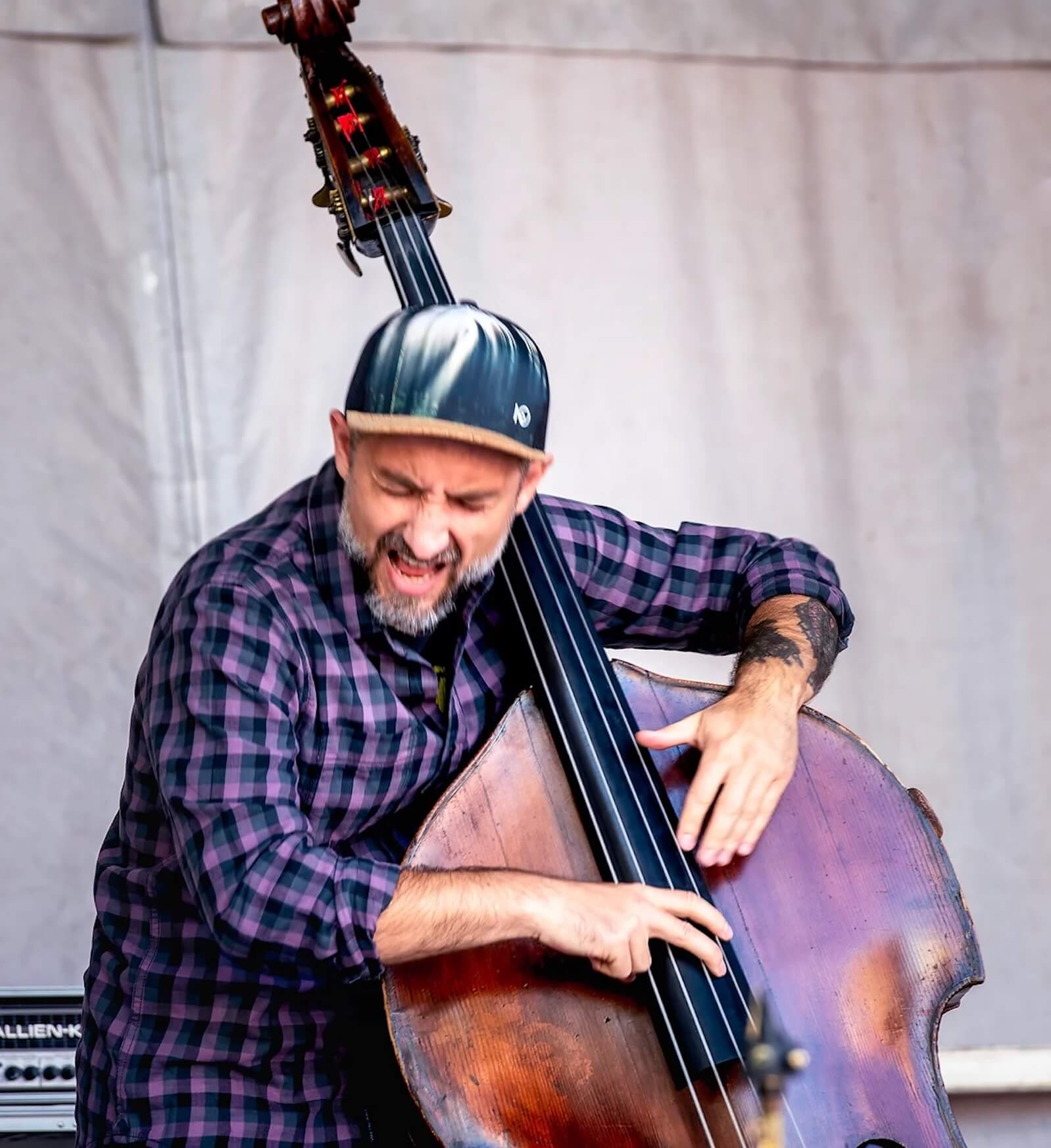 Stéphane Daimantakiou wearing a checkered shirt and hat playing his bass