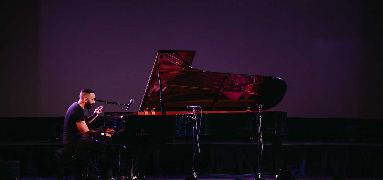 Adam Tendler on stage, playing piano in front of a purple screen.