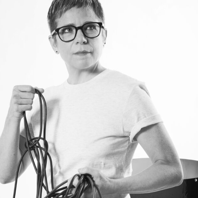 Black and white photo of Anne La Berge in a white t-shirt holding a black cable