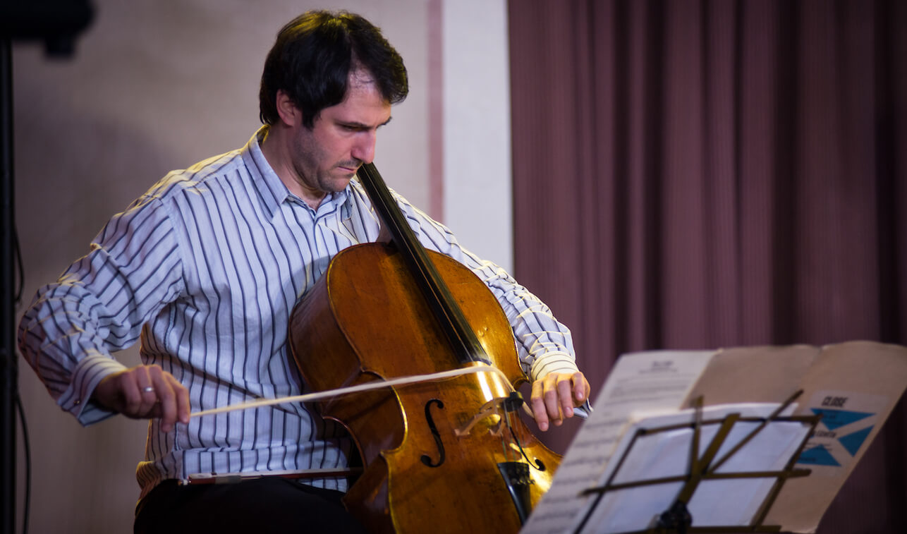 Ariel Barnes wearing a blue and white striped shirt, playing the cello