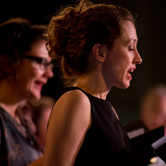 Singers, one female close up and two blurry in the background