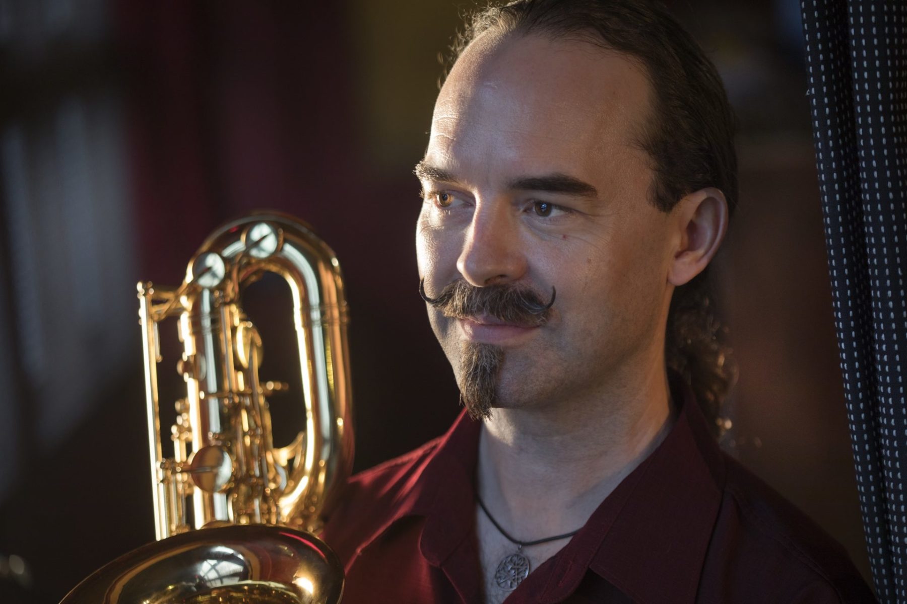 Colin MacDonald with a goatee in a red shirt posing with a saxophone