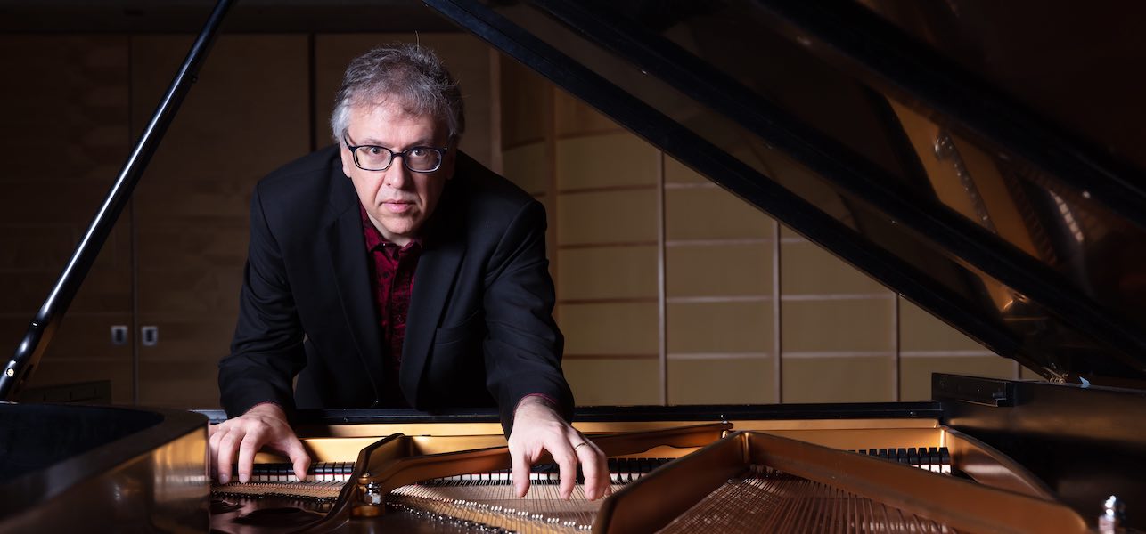 Corey Hamm standing with both hands inside an open piano
