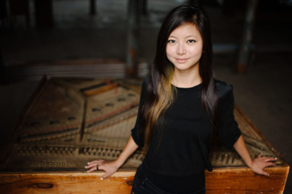 Vicky Chow in black, standing in front of an open piano