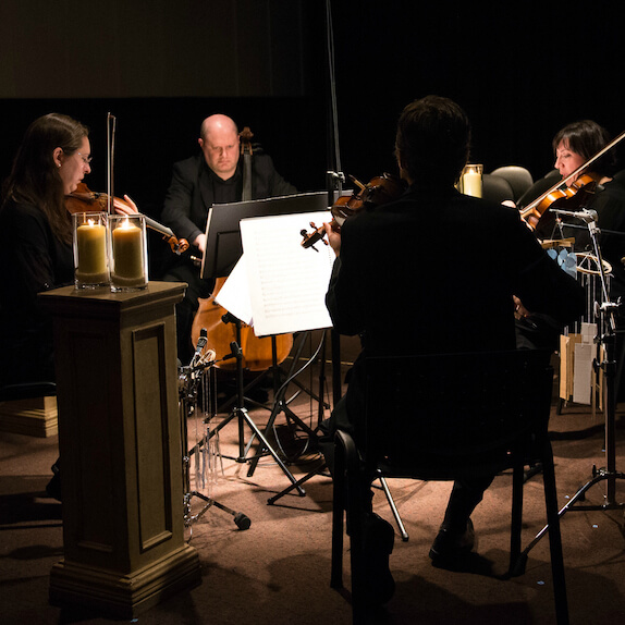 Emily Carr String Quartet performing in a square layout with candles