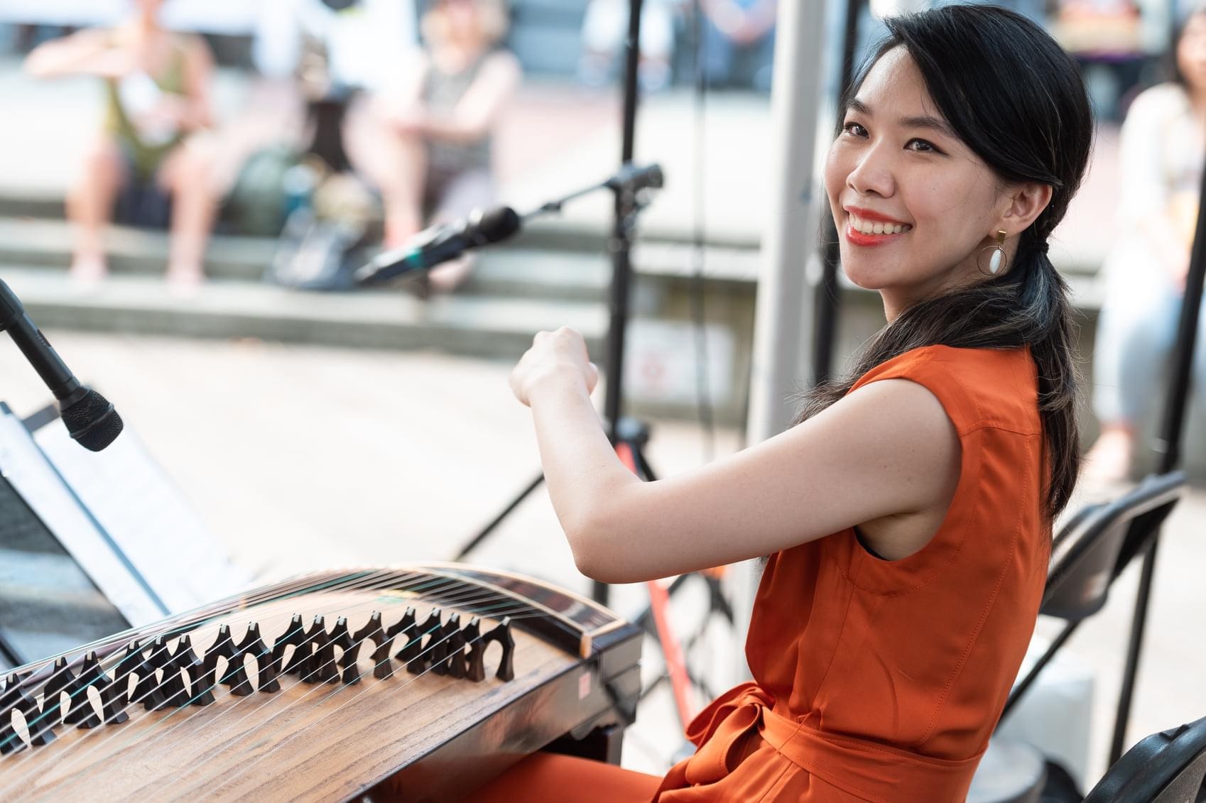 Dailin Hsieh, smiling in an orange dress, performing on the zheng