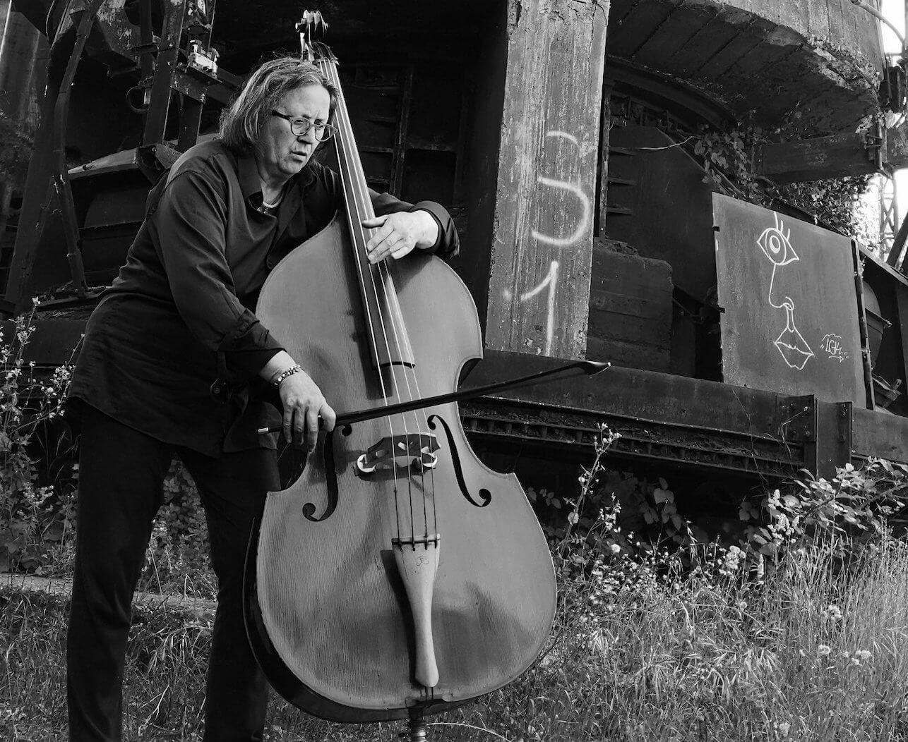 Joelle Leandre standing in front of a ruin playing her double bass
