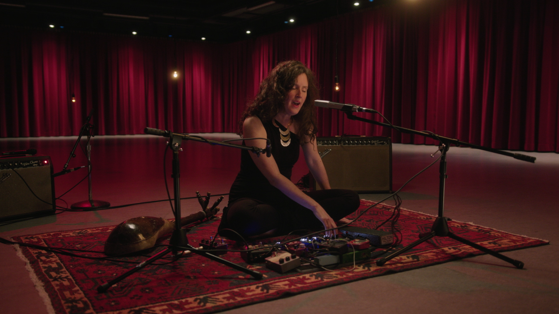 Julia Ulehla sitting on a carpet with microphones, singing in front of red curtains