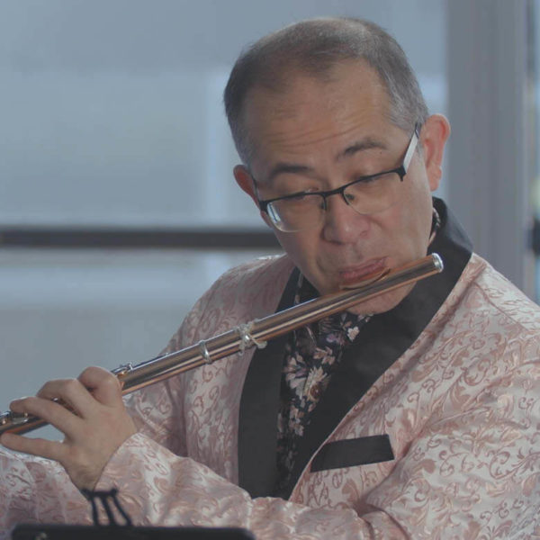 Mark Takeshi McGregor in a paisley pink jacket playing the flute