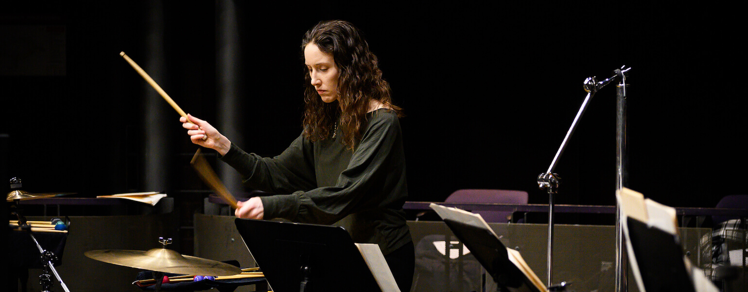 Katie Rife in a black shirt standing behind some percussion instruments