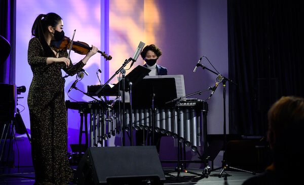 Chloe Kim wearing a sparkly black dress and black mask playing violin with Julia Chien standing behind the vibraphone wearing a black mask