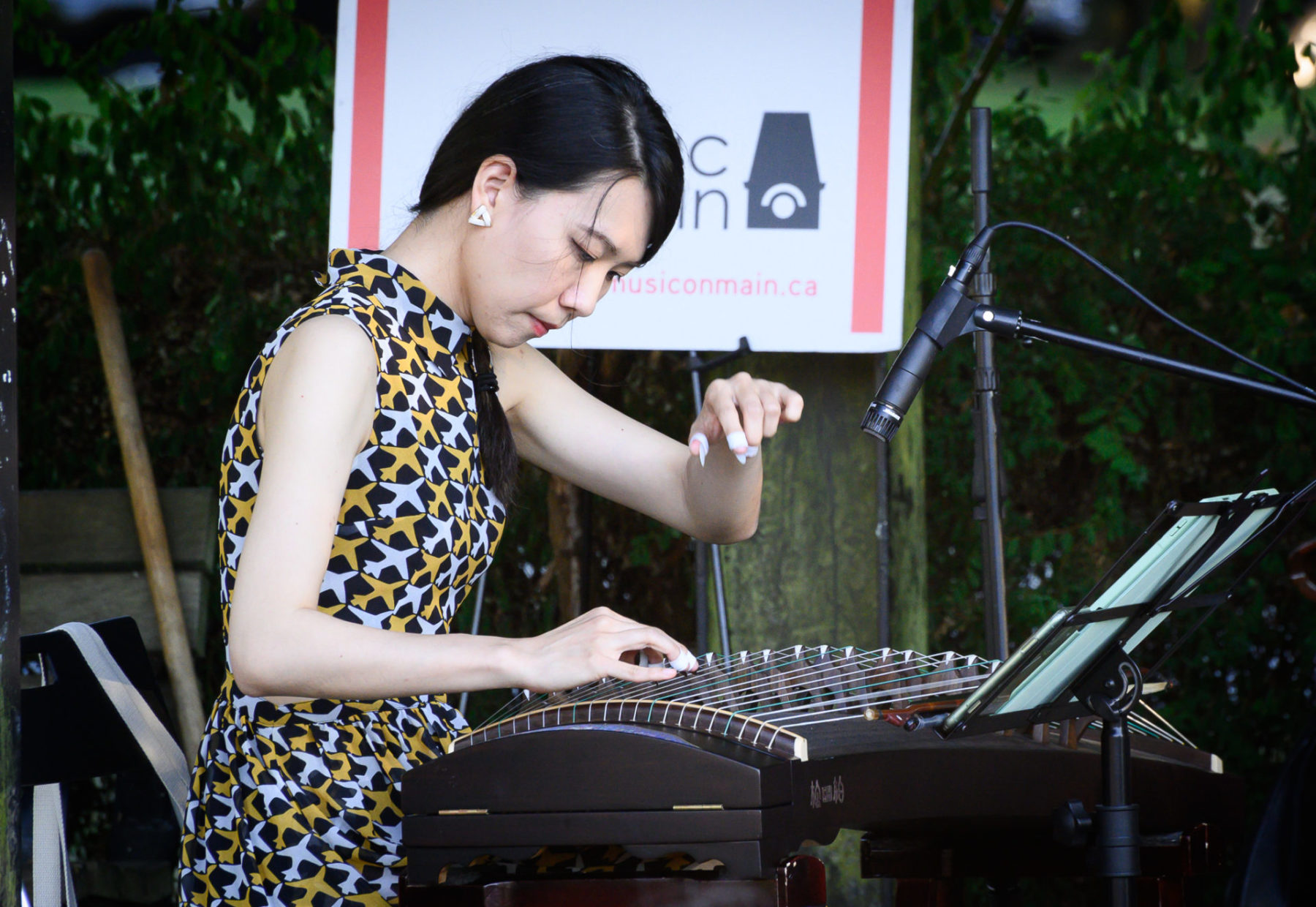 Dailin Hsieh in a dress with grey and orange planes, playing the zheng.