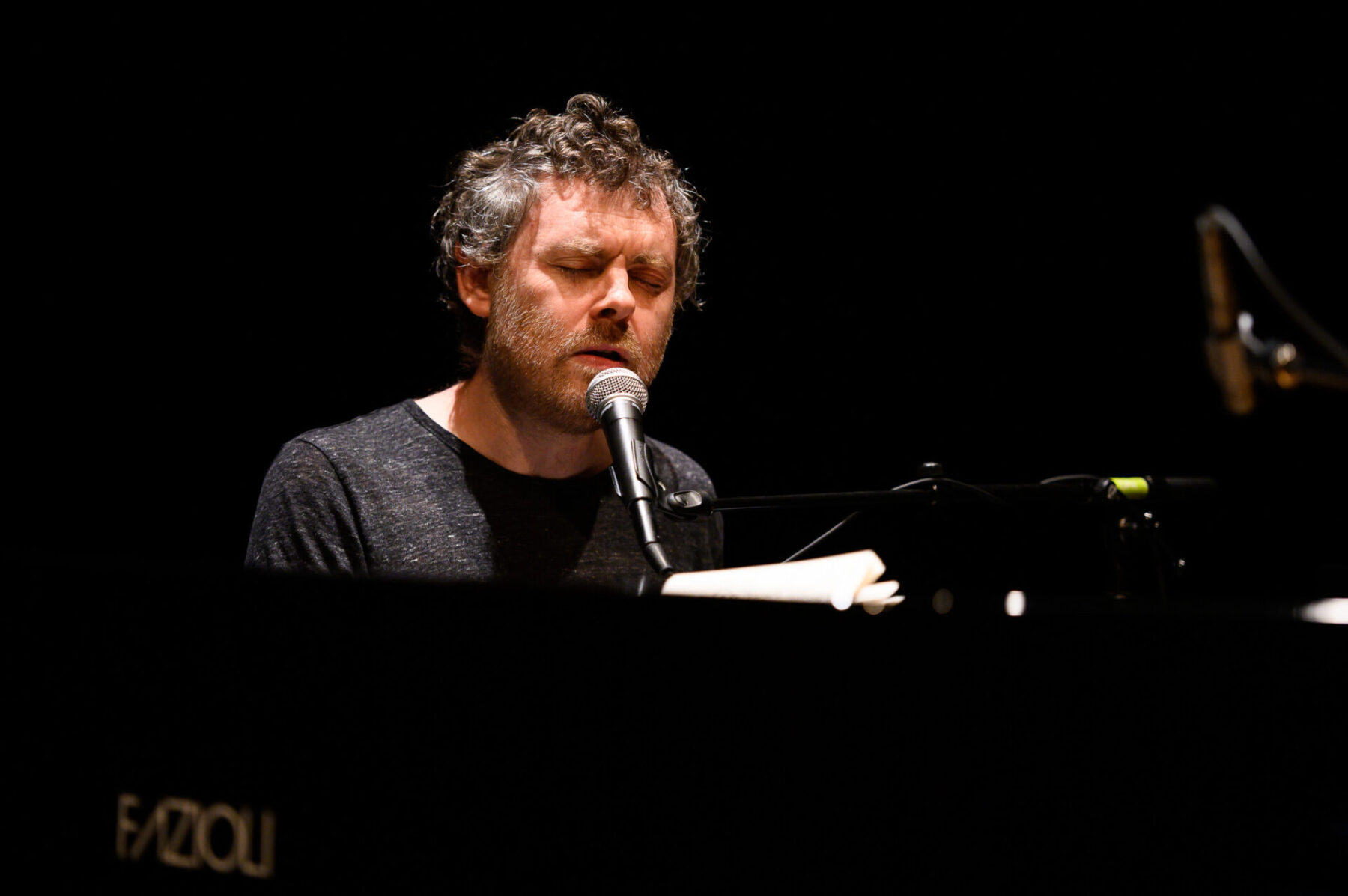 Gabriel Kahane singing into at a microphone at a piano