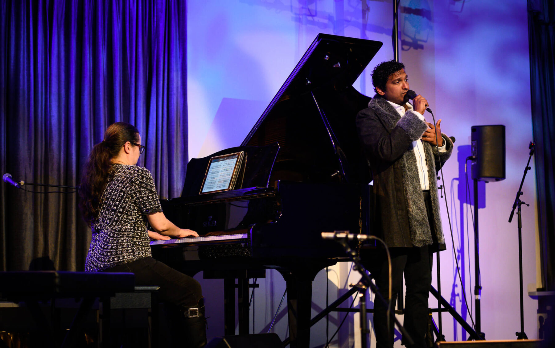 Rachel Kiyo Iwaasa on piano in a white and black shirt with Asitha Tennekoon singing in a fur rimmed coat