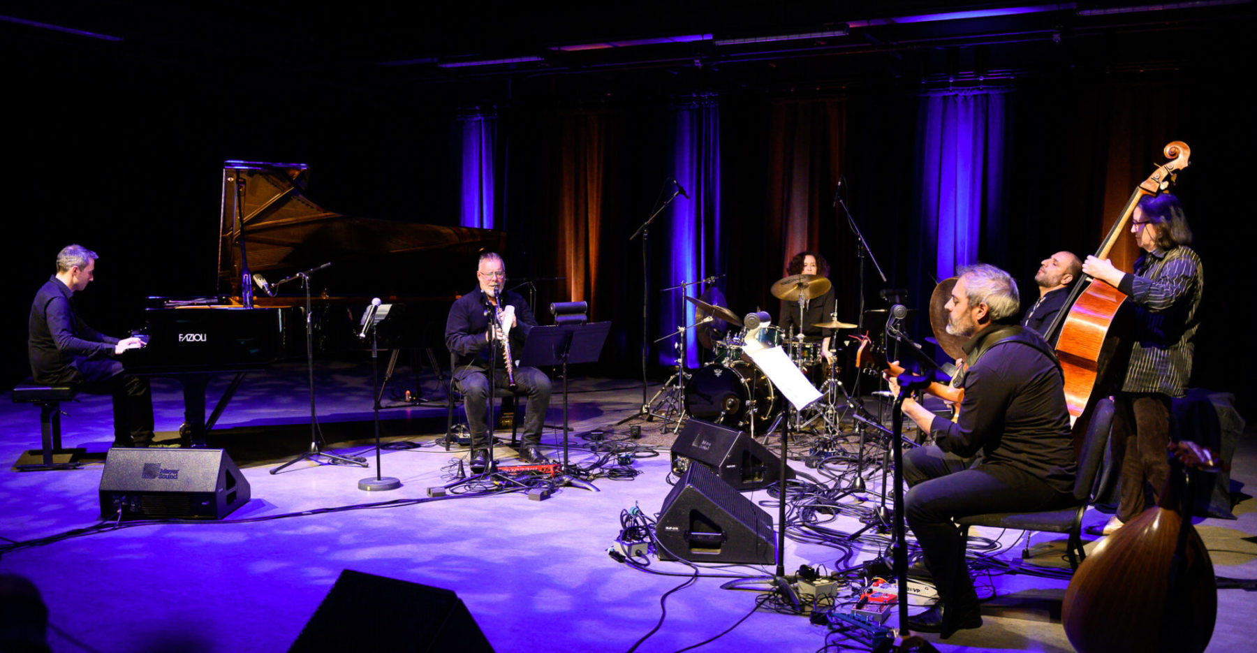 Photo of all performers of François Houle's The Secret Lives of Colour, bathed in a purple and white light