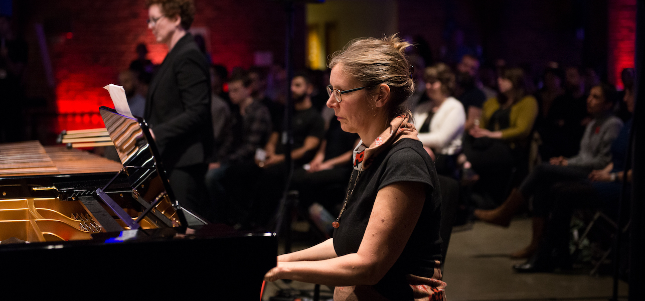 Marguerite Witvoet playing piano during a performance, with audience seating behind.