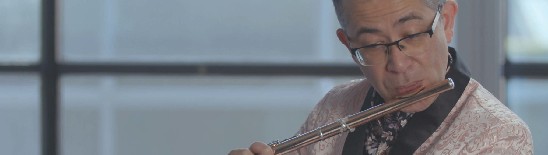 Mark Takeshi McGregor in a paisley pink jacket playing the flute