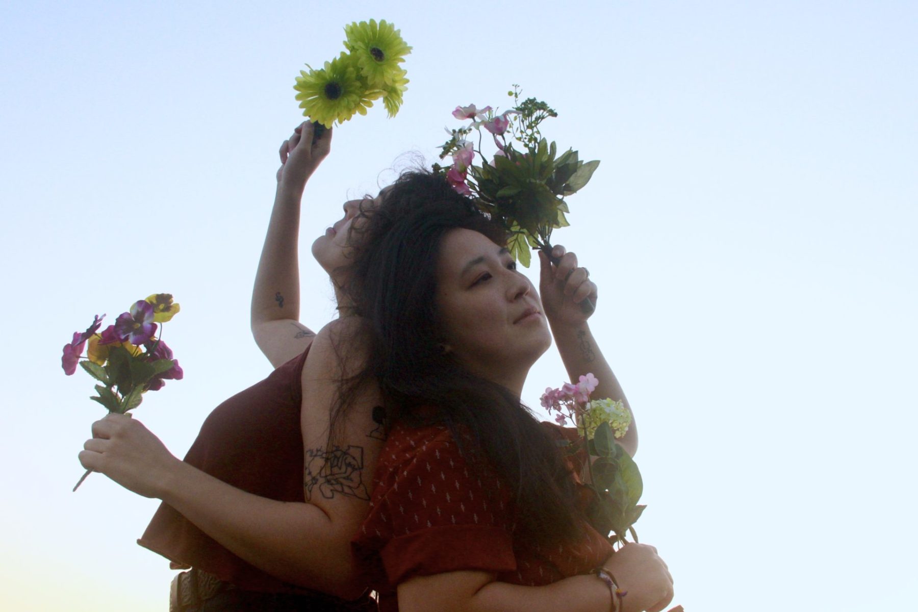 Aysha Dulong holding flowers above their head and in front of them and Cindy Kao is holding flowers at her forehead and in front of her