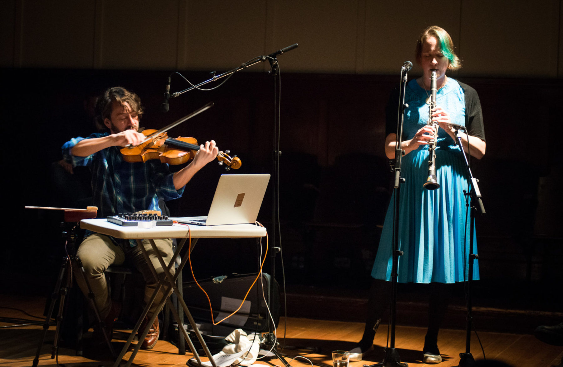 Elizabeth Lima standing on the right, wearing a bright blue dress and playing the clarinet.