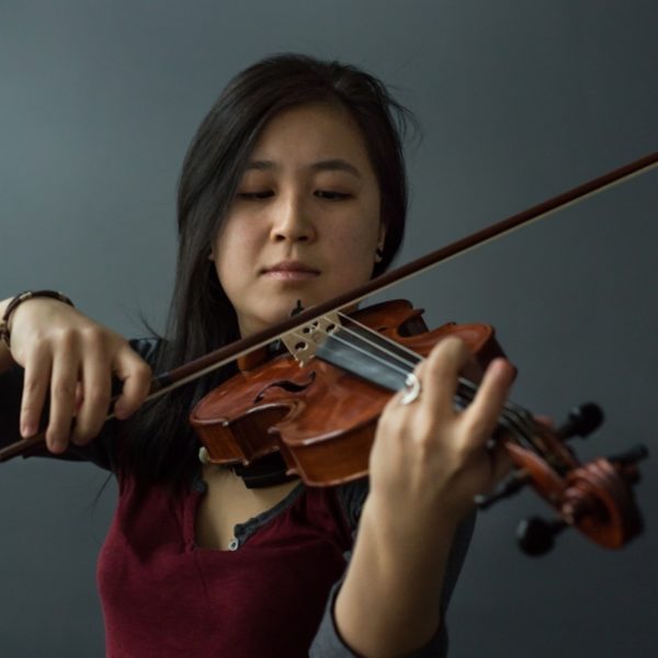 Cindy Kao in front of a grey background holding up her violin