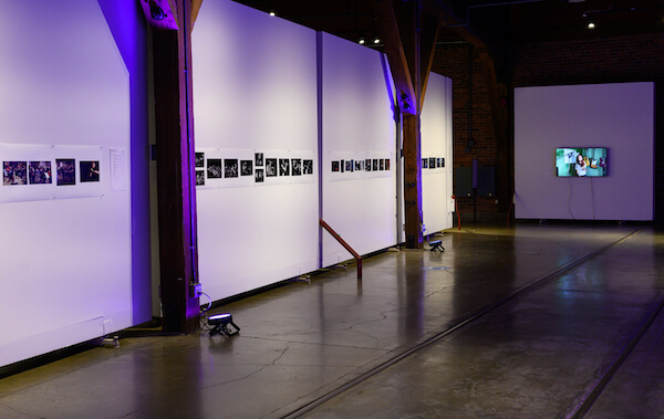 White gallery walls with wood posts show a line of images, highlighted by purple lights.